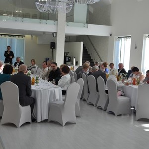 siedzące osoby przy stolikach i przemawiającego Wójta 