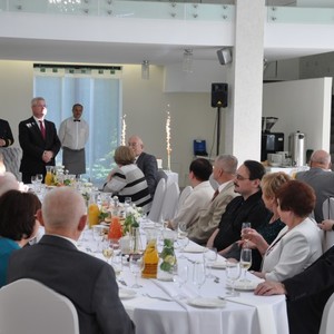 siedzące osoby przy stolikach i przemawiającego Wójta 